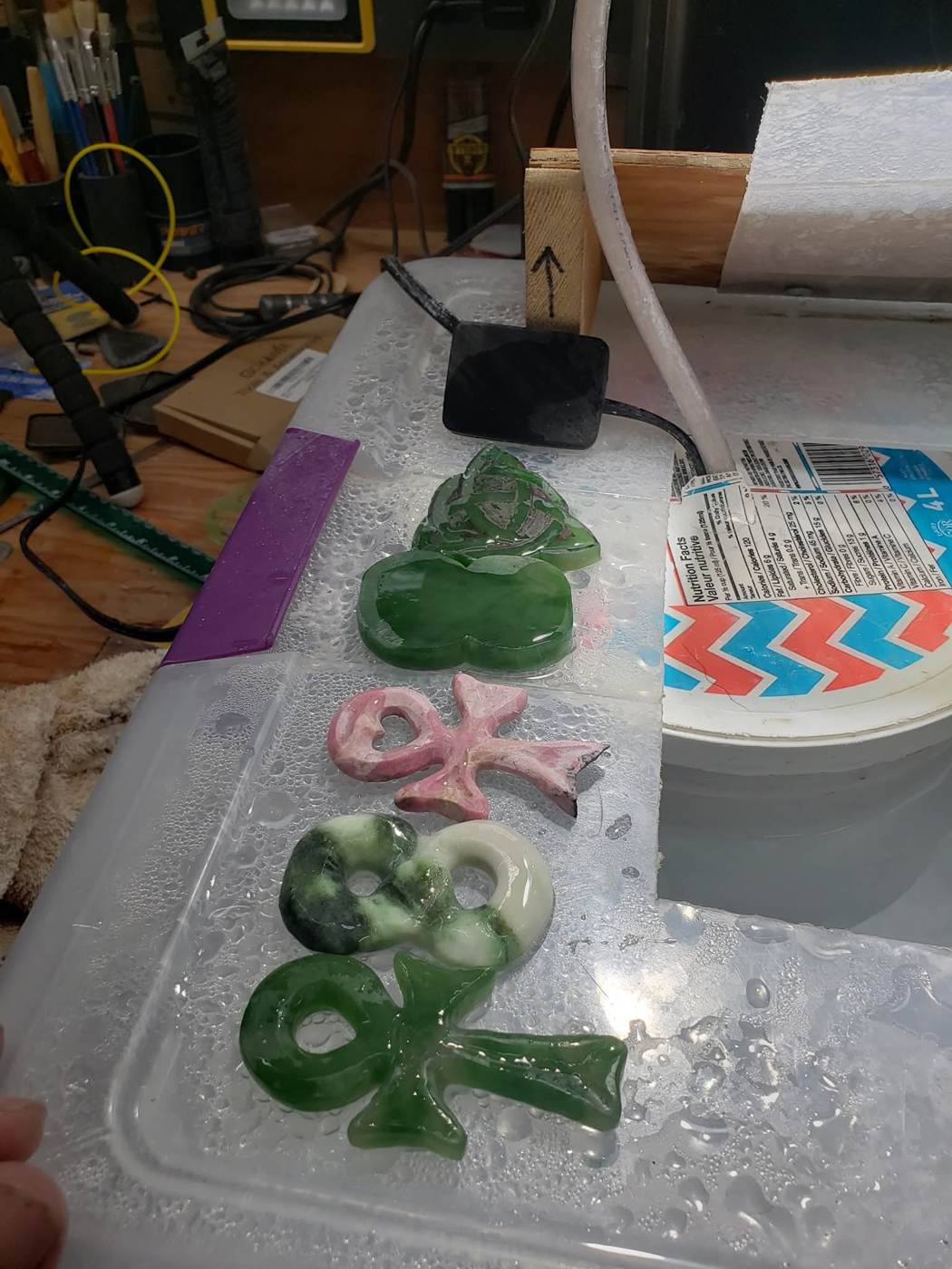Green jade pendants and a pink-and-white stone pendant on a wet lapidary tray