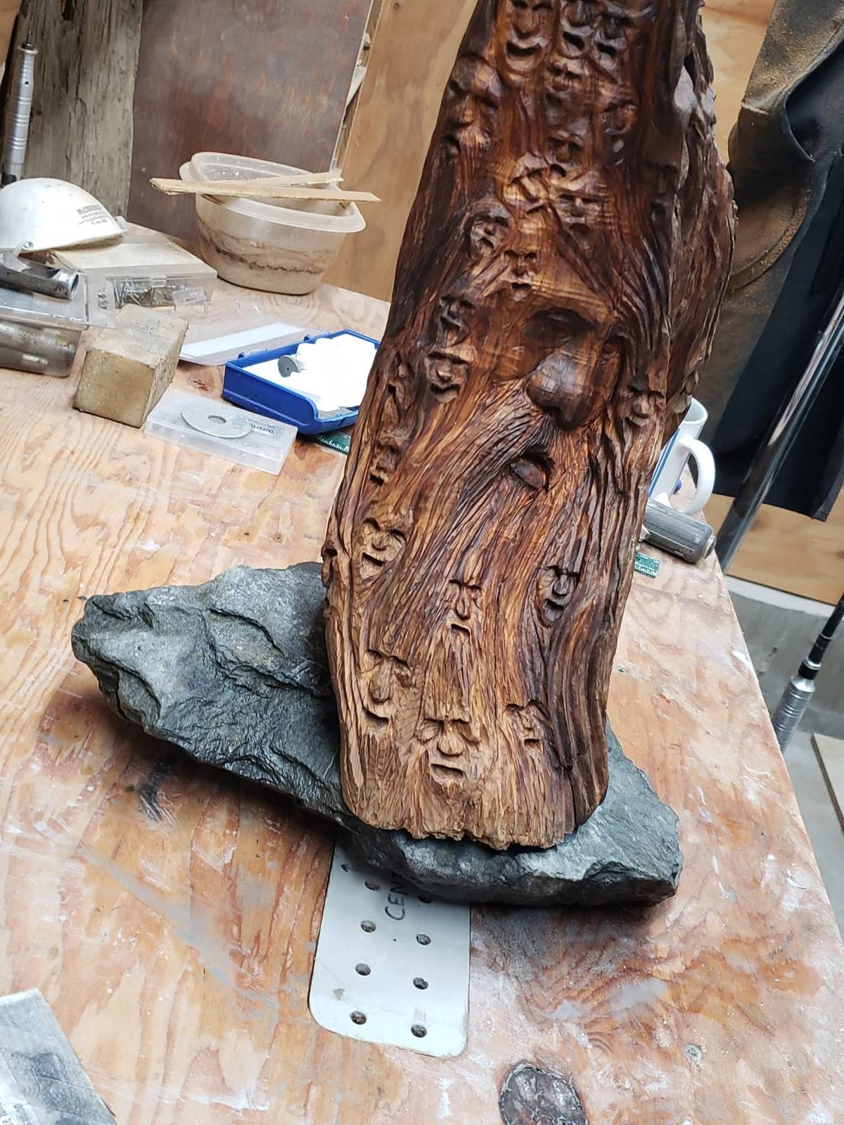 Wood spirit carving with a bearded face and dozens of smaller faces, side view